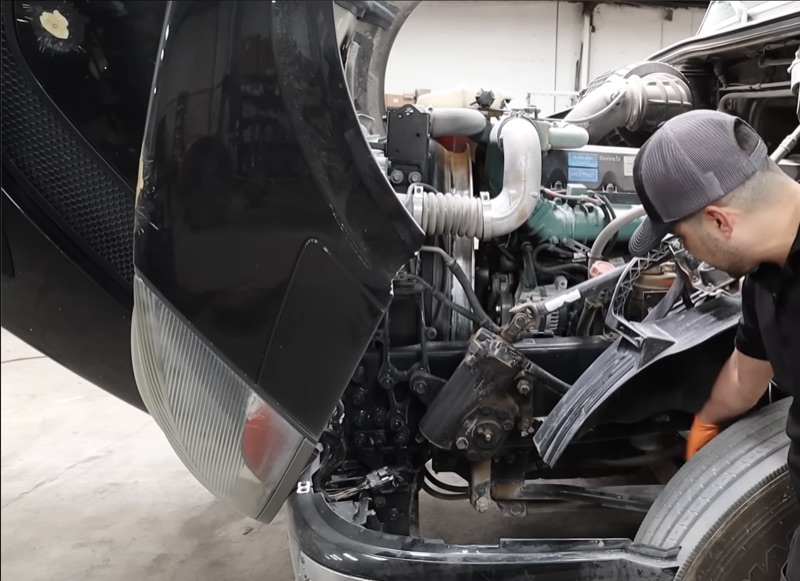 Mechanic inspecting the engine compartment of a semi truck during service