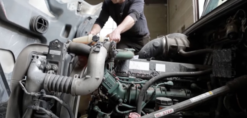 Technician working on a diesel engine with hood tilted open